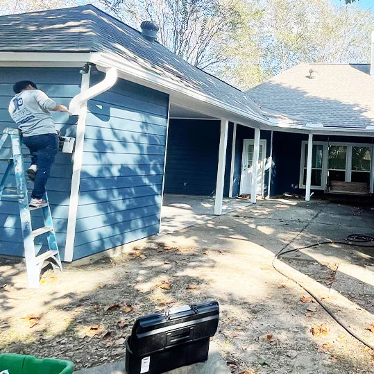 JP Professional Painters crew member on a ladder painting exterior trim of a blue house